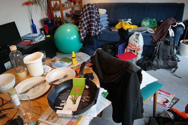a messy living room and kitchen table with dirty dishes and clutter