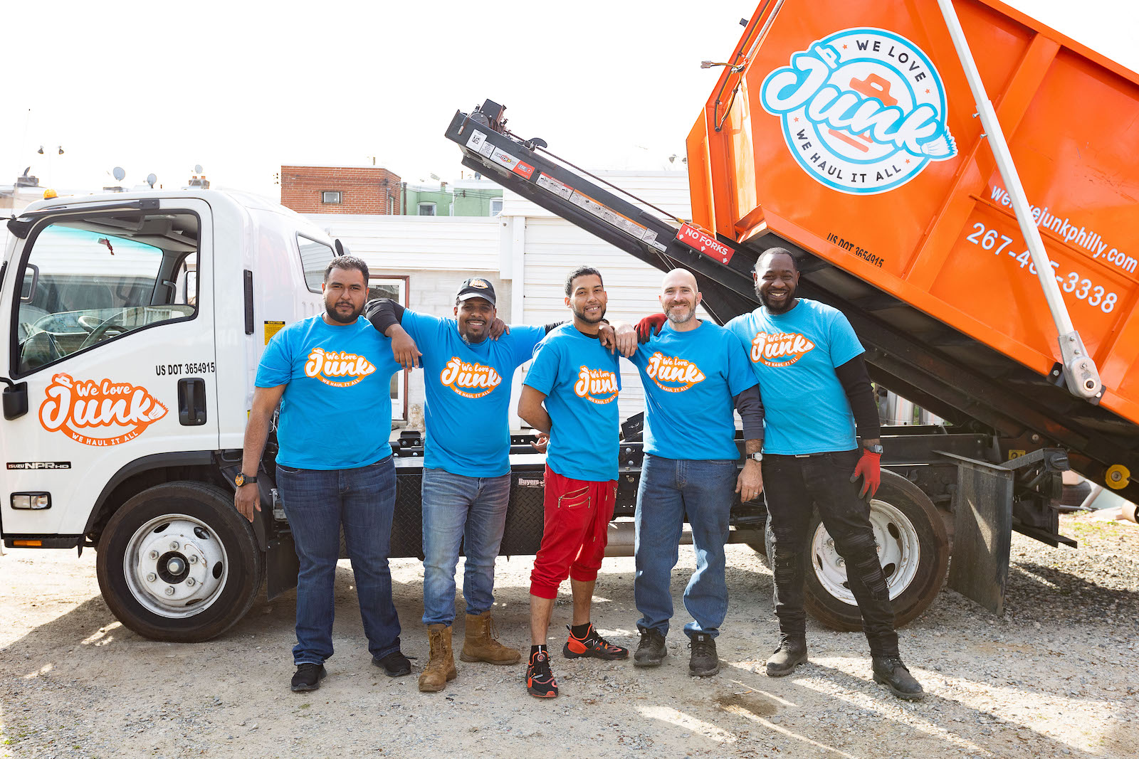 junk removal team standing together in front of branded We Love Junk truck and container