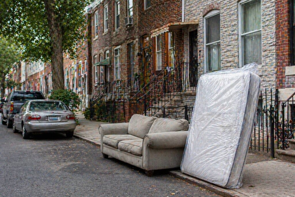 Couch and plastic-wrapped mattress placed at the curb in front of brick rowhomes for bulk item pickup